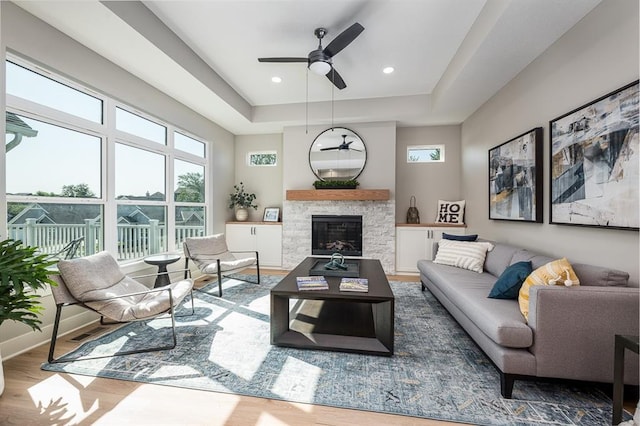 living room with recessed lighting, a raised ceiling, a stone fireplace, wood finished floors, and baseboards