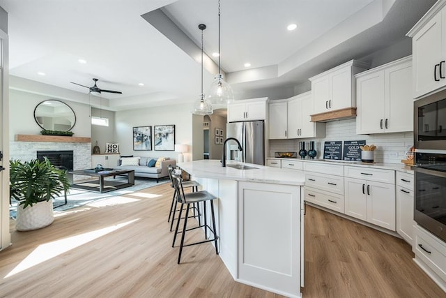 kitchen with stainless steel appliances, a raised ceiling, a sink, a stone fireplace, and light wood-type flooring