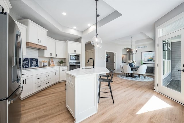 kitchen with a tray ceiling, visible vents, light wood-style flooring, appliances with stainless steel finishes, and a sink