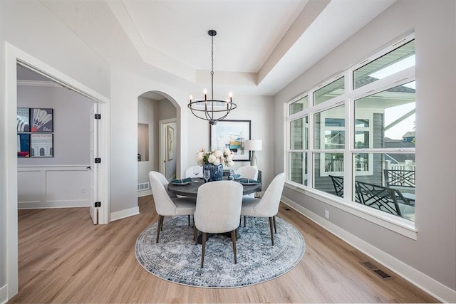 dining space with arched walkways, a chandelier, wood finished floors, visible vents, and a raised ceiling