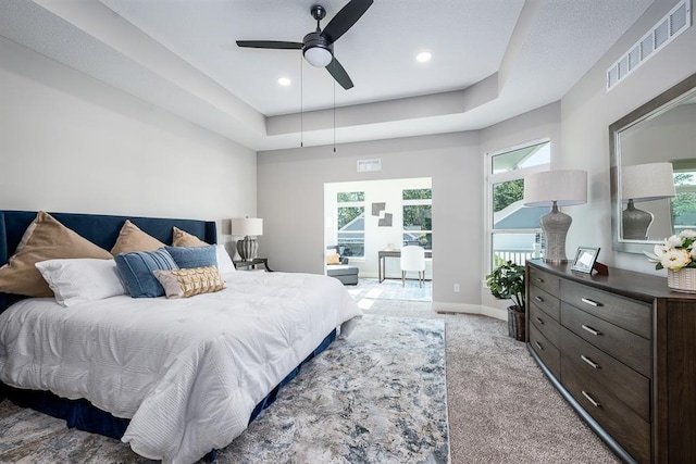 bedroom with a tray ceiling, light colored carpet, visible vents, ceiling fan, and baseboards