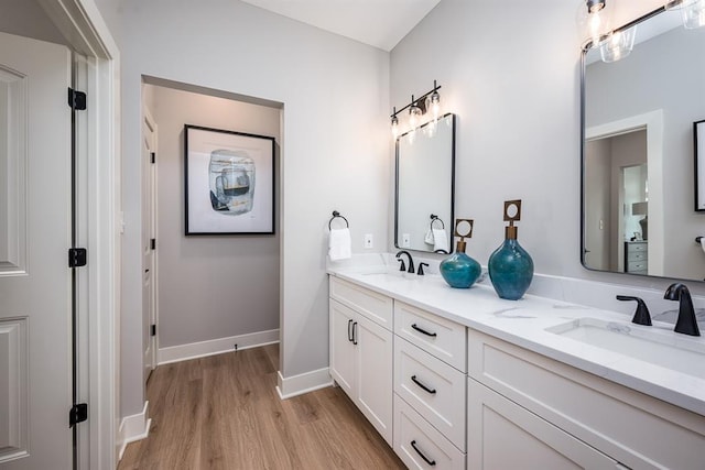 bathroom with double vanity, wood finished floors, a sink, and baseboards