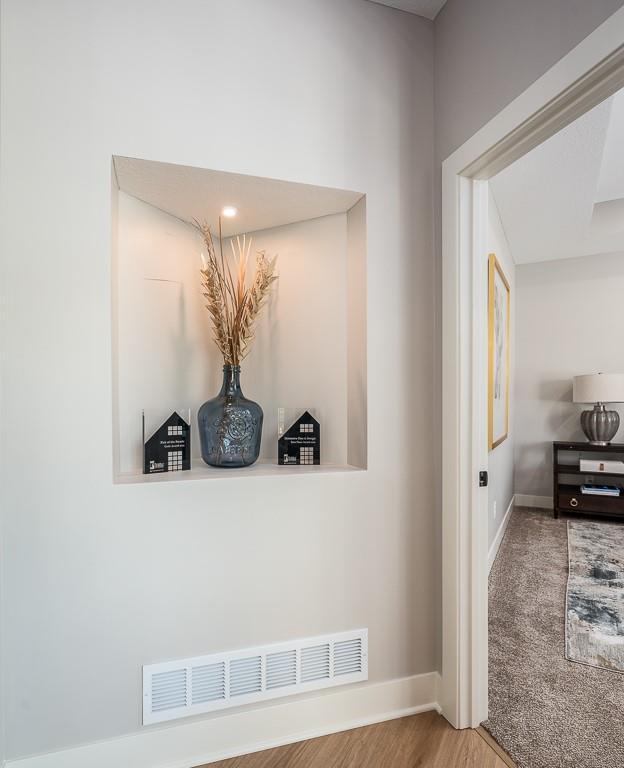 corridor featuring wood finished floors, visible vents, and baseboards