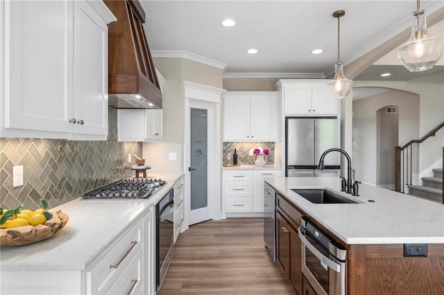 kitchen featuring custom range hood, stainless steel appliances, sink, pendant lighting, and a kitchen island with sink