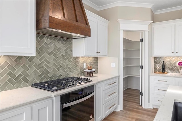 kitchen with appliances with stainless steel finishes, white cabinetry, custom range hood, and tasteful backsplash