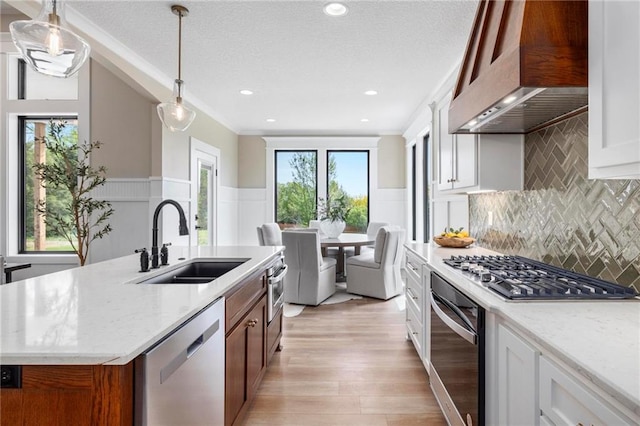 kitchen with sink, range hood, white cabinetry, and a kitchen island with sink