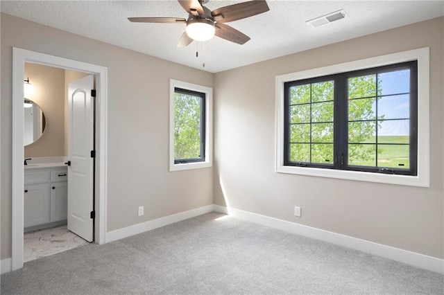 unfurnished bedroom featuring ceiling fan, ensuite bathroom, light carpet, and a textured ceiling