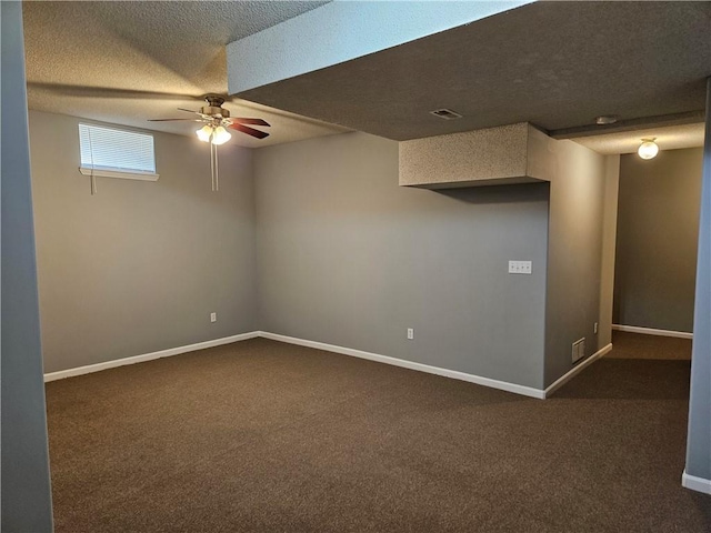 basement with visible vents, baseboards, a ceiling fan, dark colored carpet, and a textured ceiling