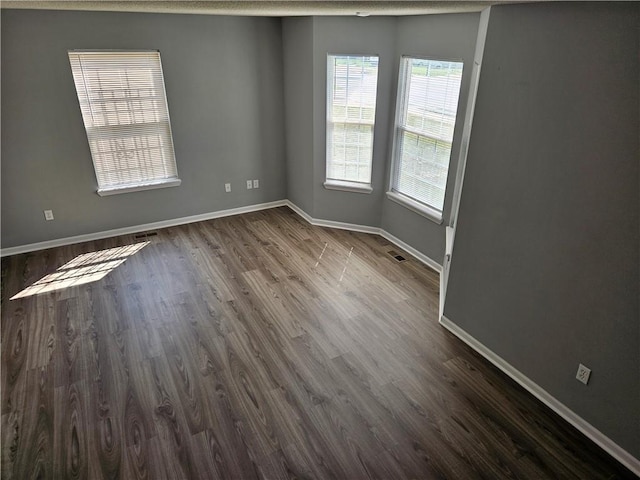 unfurnished room with visible vents, baseboards, and dark wood-type flooring