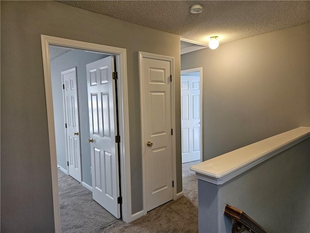 hall with a textured ceiling, carpet flooring, and baseboards