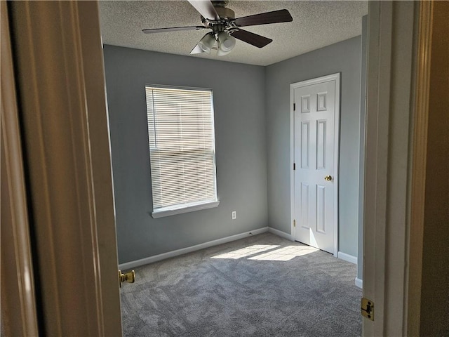 carpeted spare room with a ceiling fan, baseboards, and a textured ceiling