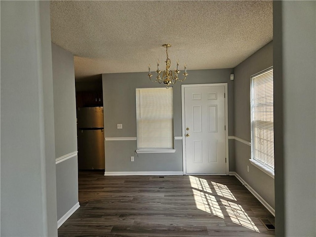 unfurnished dining area featuring baseboards, a textured ceiling, a chandelier, and dark wood-style flooring