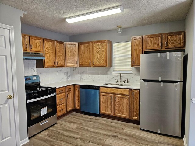 kitchen featuring under cabinet range hood, stainless steel appliances, a sink, and light countertops