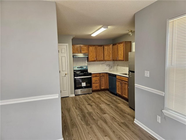 kitchen with under cabinet range hood, dark wood-style flooring, appliances with stainless steel finishes, tasteful backsplash, and brown cabinetry