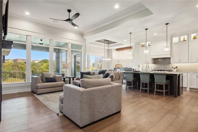 living room featuring ceiling fan with notable chandelier, ornamental molding, a tray ceiling, and light hardwood / wood-style floors