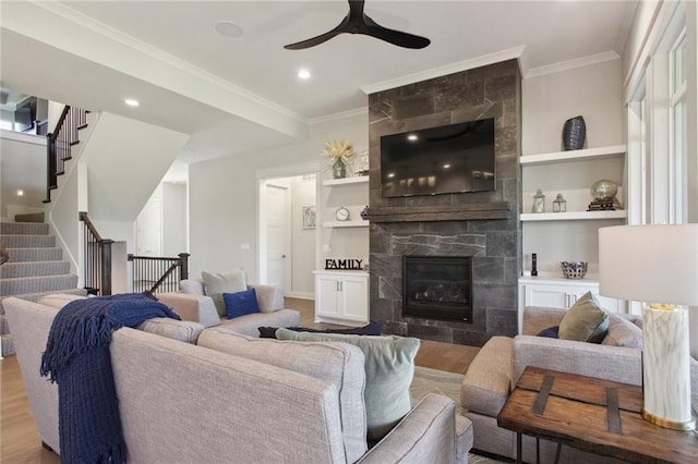 living room featuring a fireplace, built in features, crown molding, hardwood / wood-style flooring, and ceiling fan