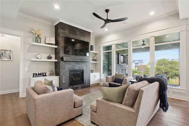 living room with a tiled fireplace, ornamental molding, hardwood / wood-style floors, and ceiling fan