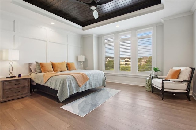 bedroom with hardwood / wood-style floors, ceiling fan, a tray ceiling, and crown molding