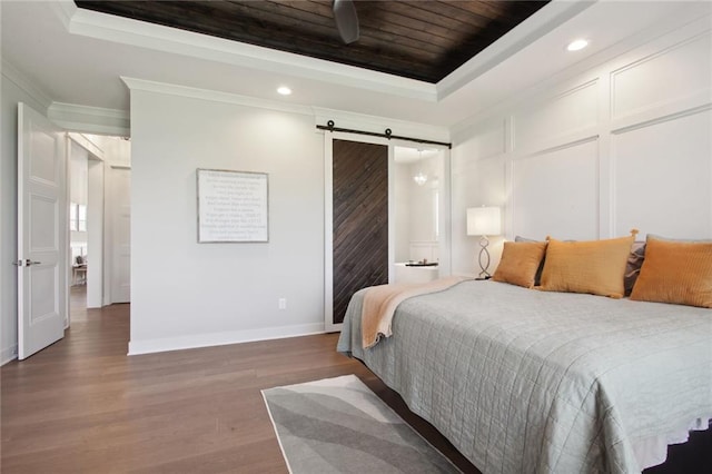 bedroom with a barn door, ornamental molding, wood-type flooring, and a tray ceiling