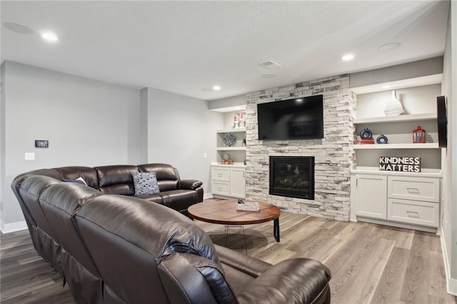 living room with a textured ceiling, built in features, hardwood / wood-style flooring, and a stone fireplace