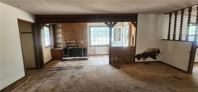 unfurnished living room featuring a textured ceiling, plenty of natural light, a stone fireplace, and carpet flooring