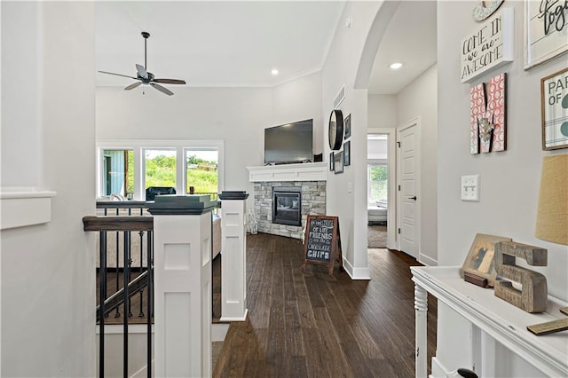 interior space with dark wood-type flooring, crown molding, a fireplace, and ceiling fan