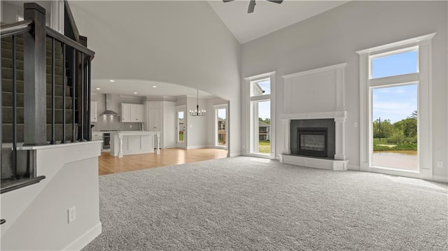 unfurnished living room featuring light carpet, ceiling fan with notable chandelier, and high vaulted ceiling