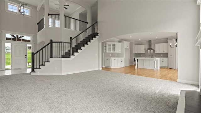 unfurnished living room featuring ceiling fan, a towering ceiling, sink, and light colored carpet