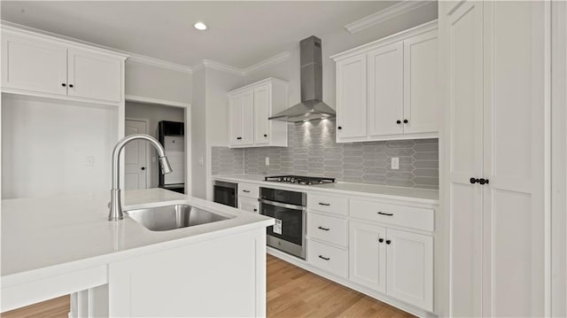 kitchen with sink, stainless steel appliances, white cabinets, a center island with sink, and wall chimney exhaust hood