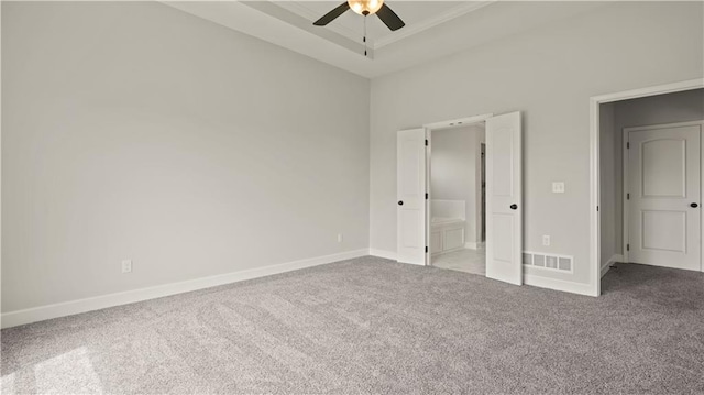 unfurnished bedroom with crown molding, ensuite bath, light carpet, a tray ceiling, and ceiling fan