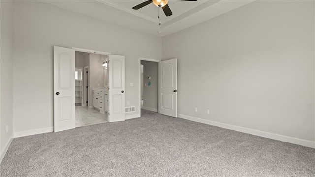 unfurnished bedroom with ensuite bath, light colored carpet, a raised ceiling, a towering ceiling, and ceiling fan