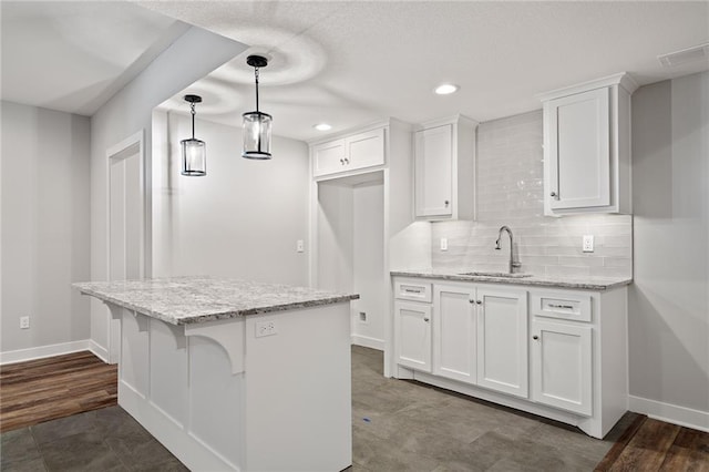 kitchen with visible vents, backsplash, white cabinetry, a sink, and baseboards