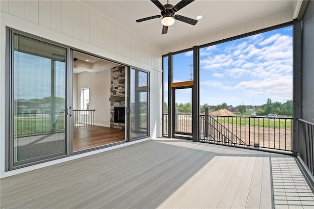 unfurnished sunroom with ceiling fan and a fireplace