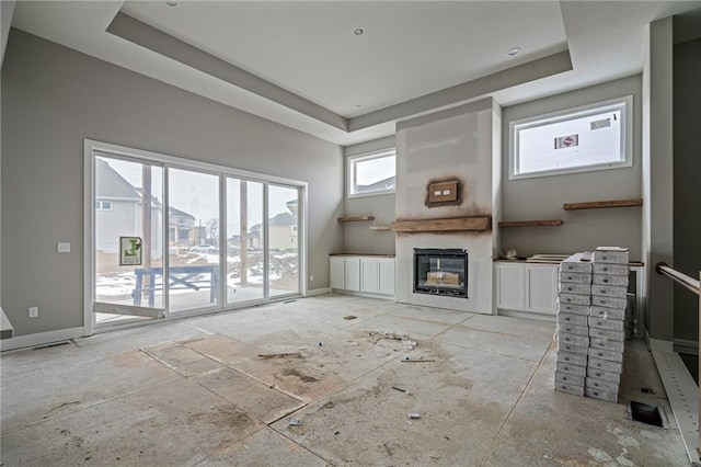 unfurnished living room featuring a glass covered fireplace, a raised ceiling, and baseboards