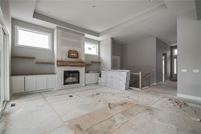 unfurnished living room with baseboards, a tray ceiling, and a glass covered fireplace