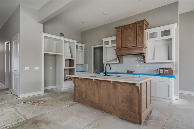 kitchen featuring an island with sink, glass insert cabinets, decorative backsplash, and a sink