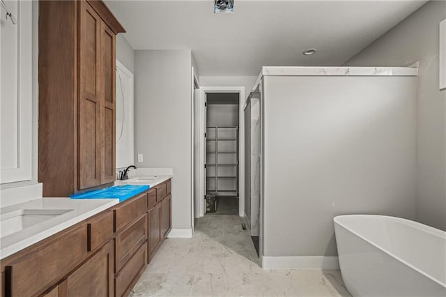 bathroom featuring marble finish floor, baseboards, a freestanding tub, and a sink