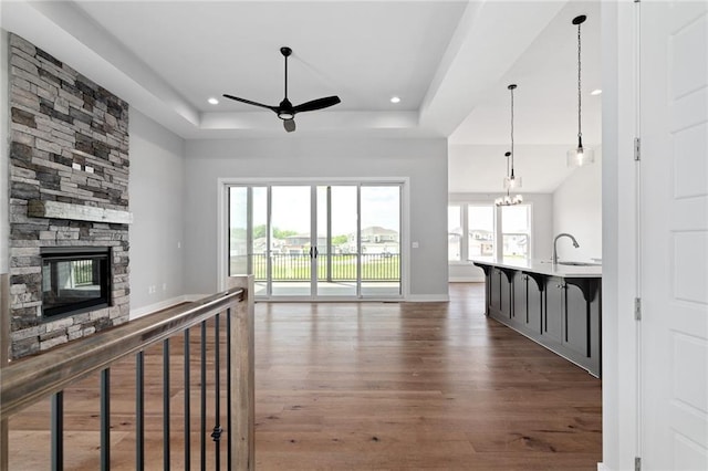 unfurnished living room with a fireplace, a raised ceiling, a sink, wood finished floors, and ceiling fan with notable chandelier