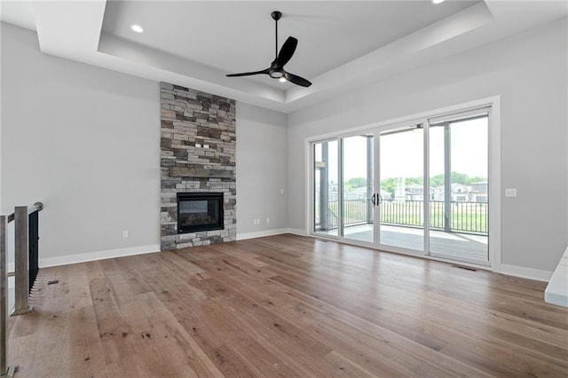 unfurnished living room with baseboards, hardwood / wood-style flooring, ceiling fan, a tray ceiling, and a fireplace