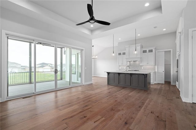 kitchen with tasteful backsplash, white cabinetry, a center island with sink, and hardwood / wood-style flooring