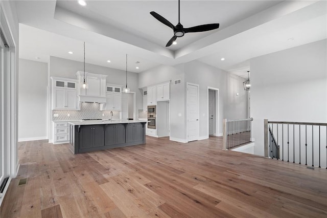 kitchen with tasteful backsplash, visible vents, white cabinets, light countertops, and light wood-style floors