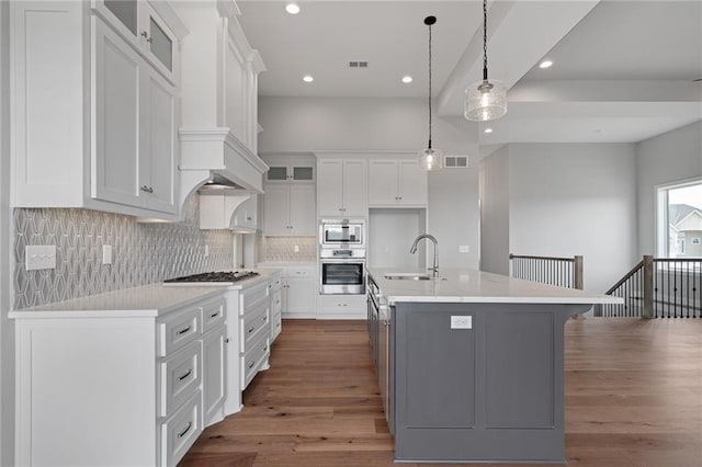 kitchen with wood finished floors, a sink, white cabinets, appliances with stainless steel finishes, and backsplash