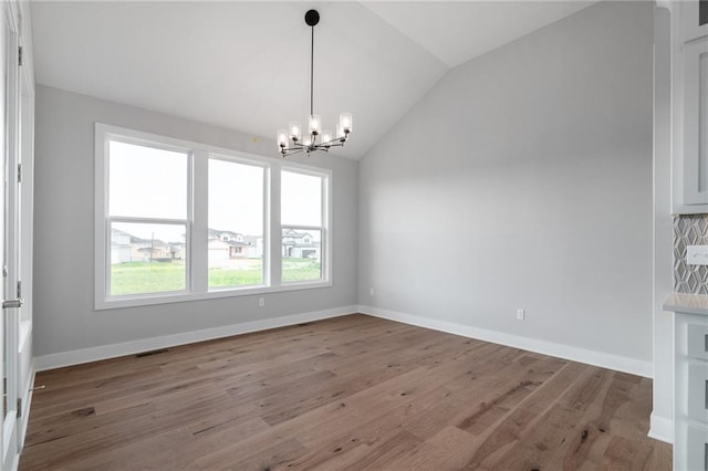 unfurnished dining area with wood finished floors, visible vents, baseboards, vaulted ceiling, and an inviting chandelier