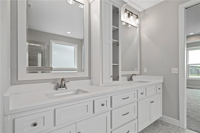 bathroom featuring double vanity, tiled shower, a sink, and baseboards