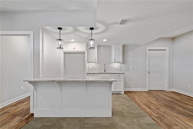 kitchen featuring a breakfast bar area, wood finished floors, visible vents, white cabinets, and backsplash