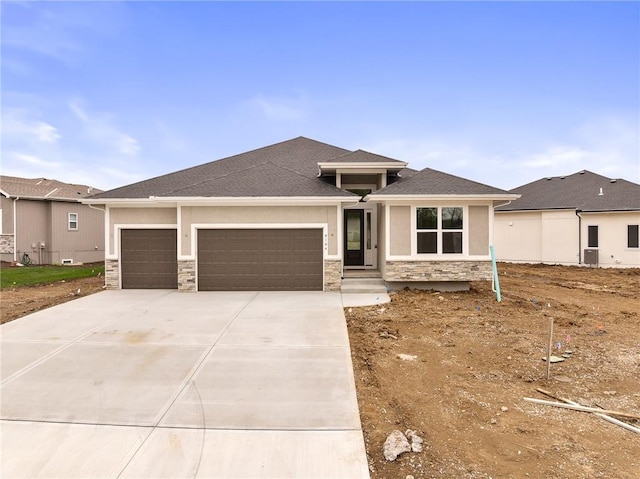 prairie-style home with stone siding, roof with shingles, stucco siding, an attached garage, and driveway