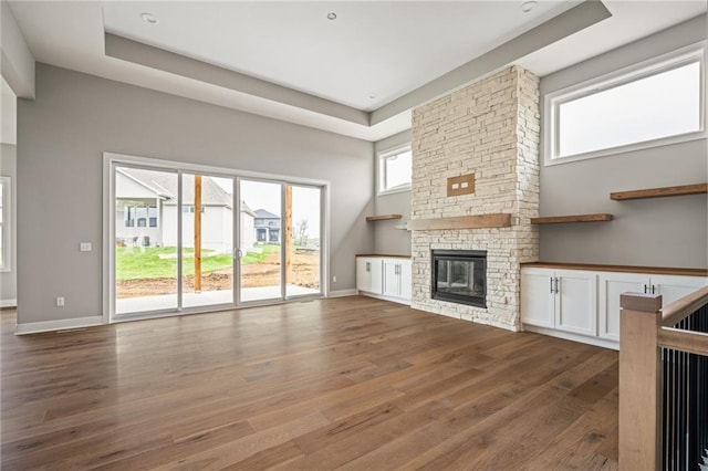 unfurnished living room featuring baseboards, wood finished floors, a raised ceiling, and a fireplace
