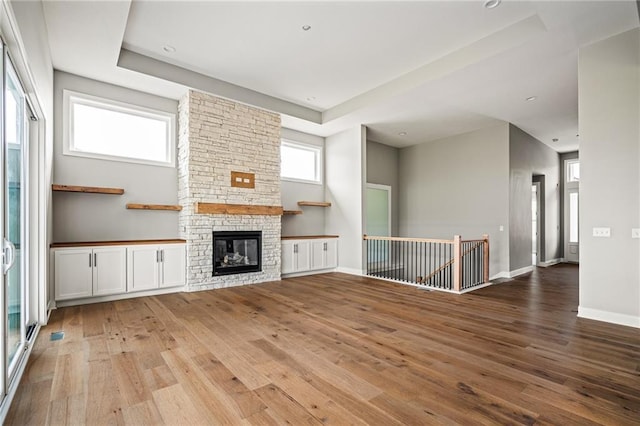 unfurnished living room featuring baseboards, a raised ceiling, a fireplace, and hardwood / wood-style floors