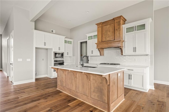kitchen with decorative backsplash, a kitchen island with sink, appliances with stainless steel finishes, a sink, and light countertops