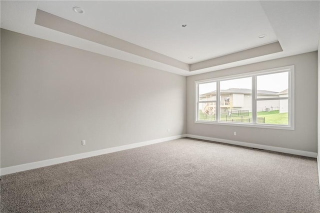 carpeted spare room with a tray ceiling and baseboards